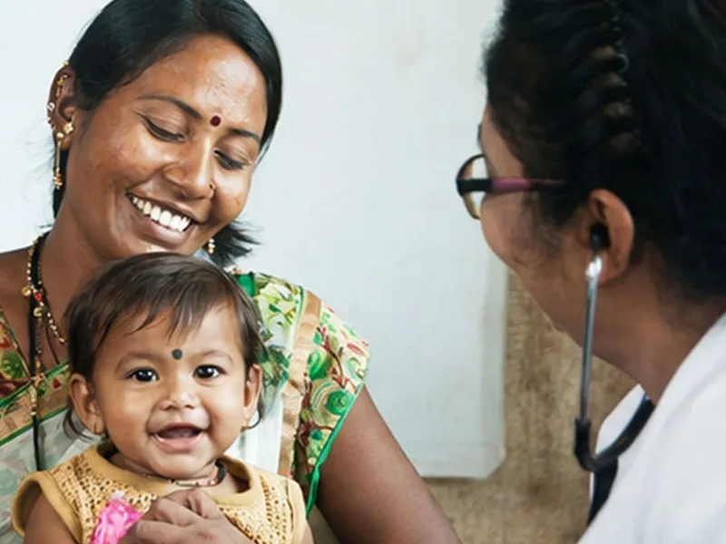 A clinician examining a smiling infant held by their mother