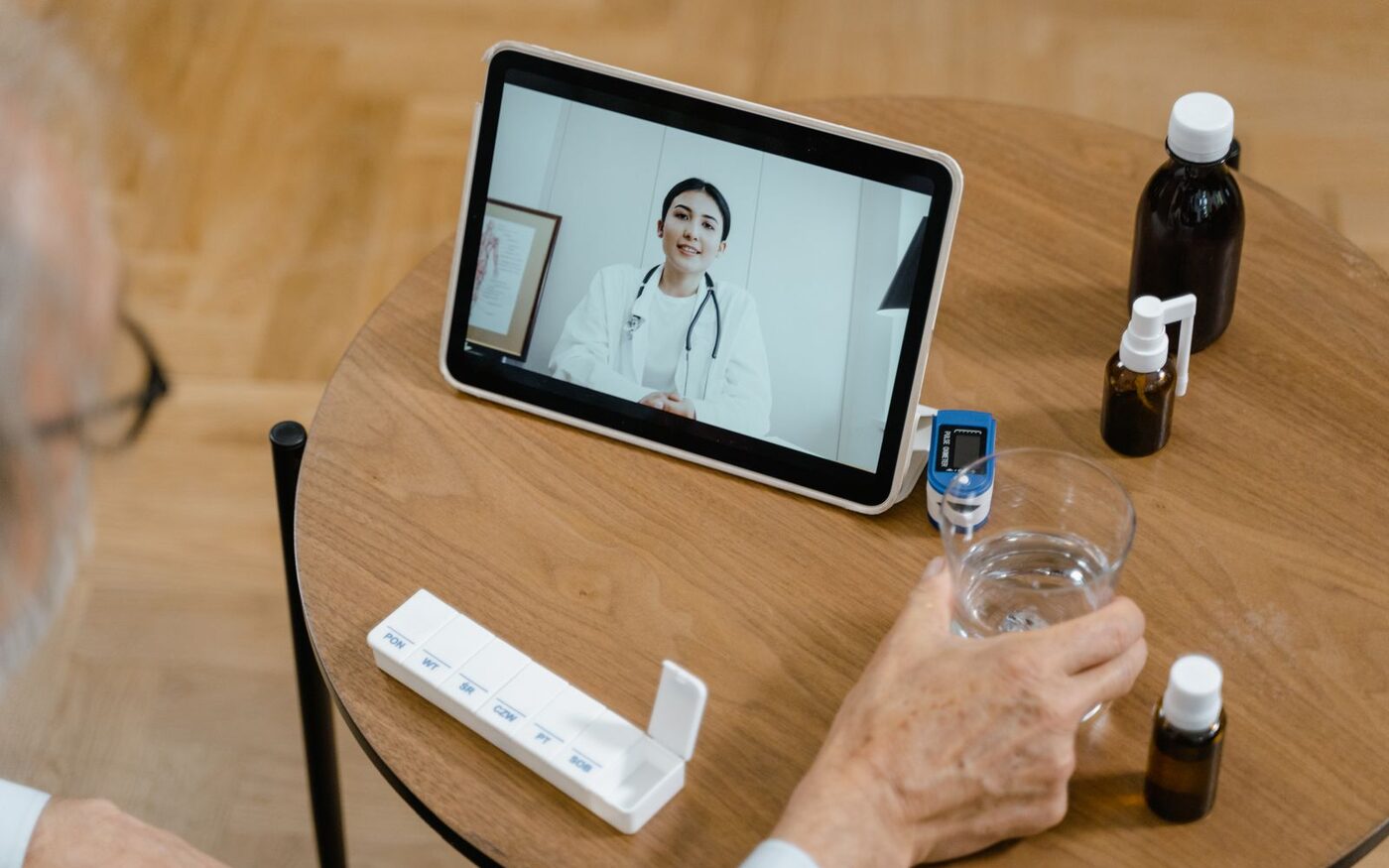 A patient’s hands beside a tablet showing a doctor during a video consultation